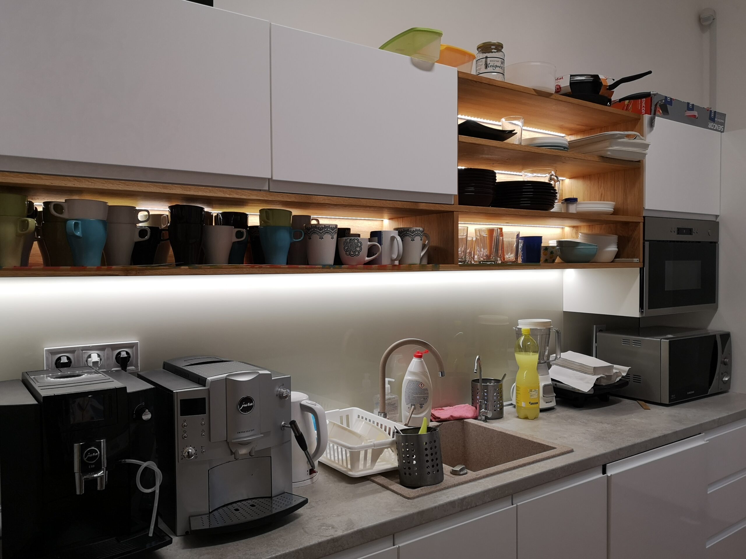 A kitchen with many glasses, plates. There are also microwave, cofee-maker.