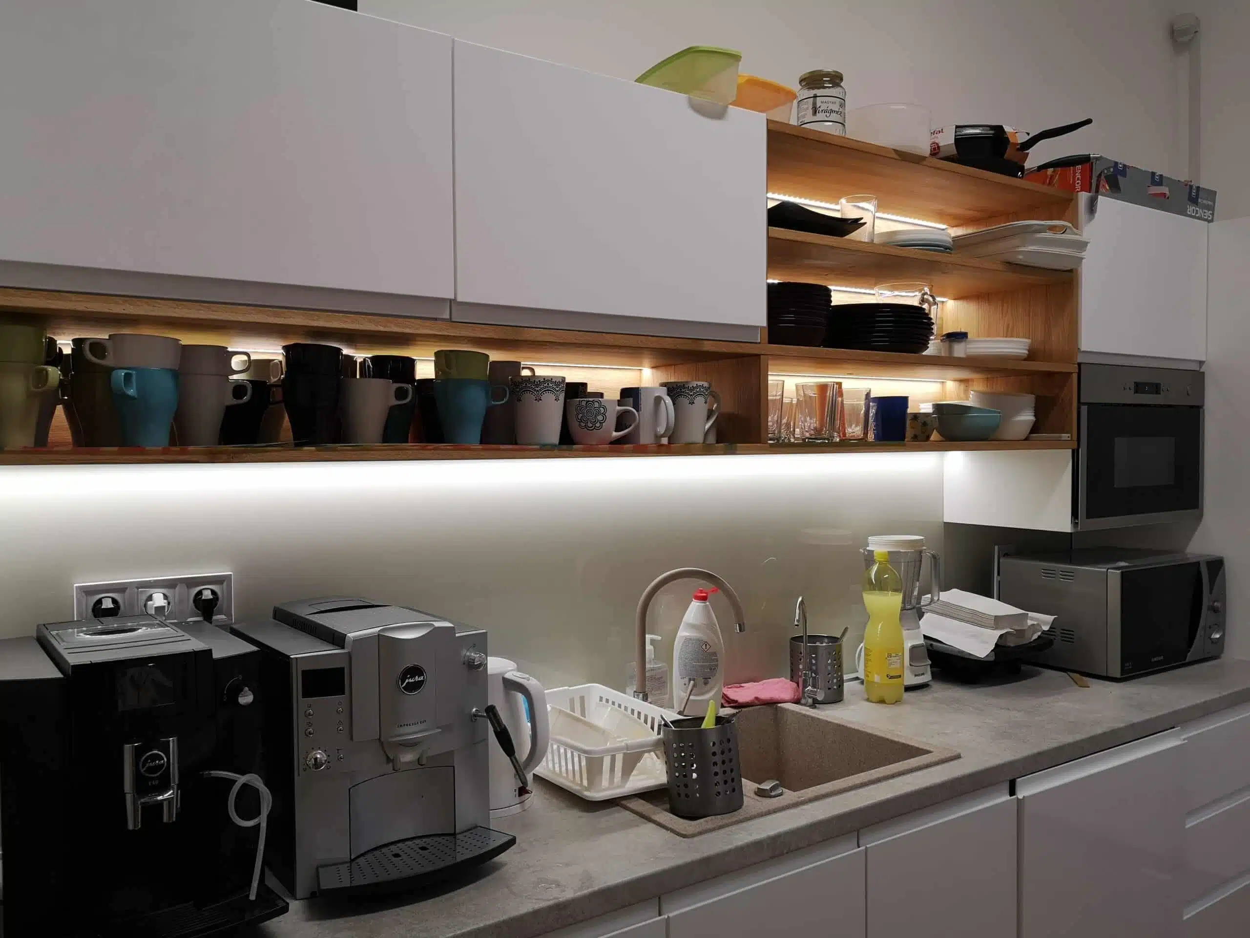 A kitchen with many glasses, plates. There are also microwave, cofee-maker.