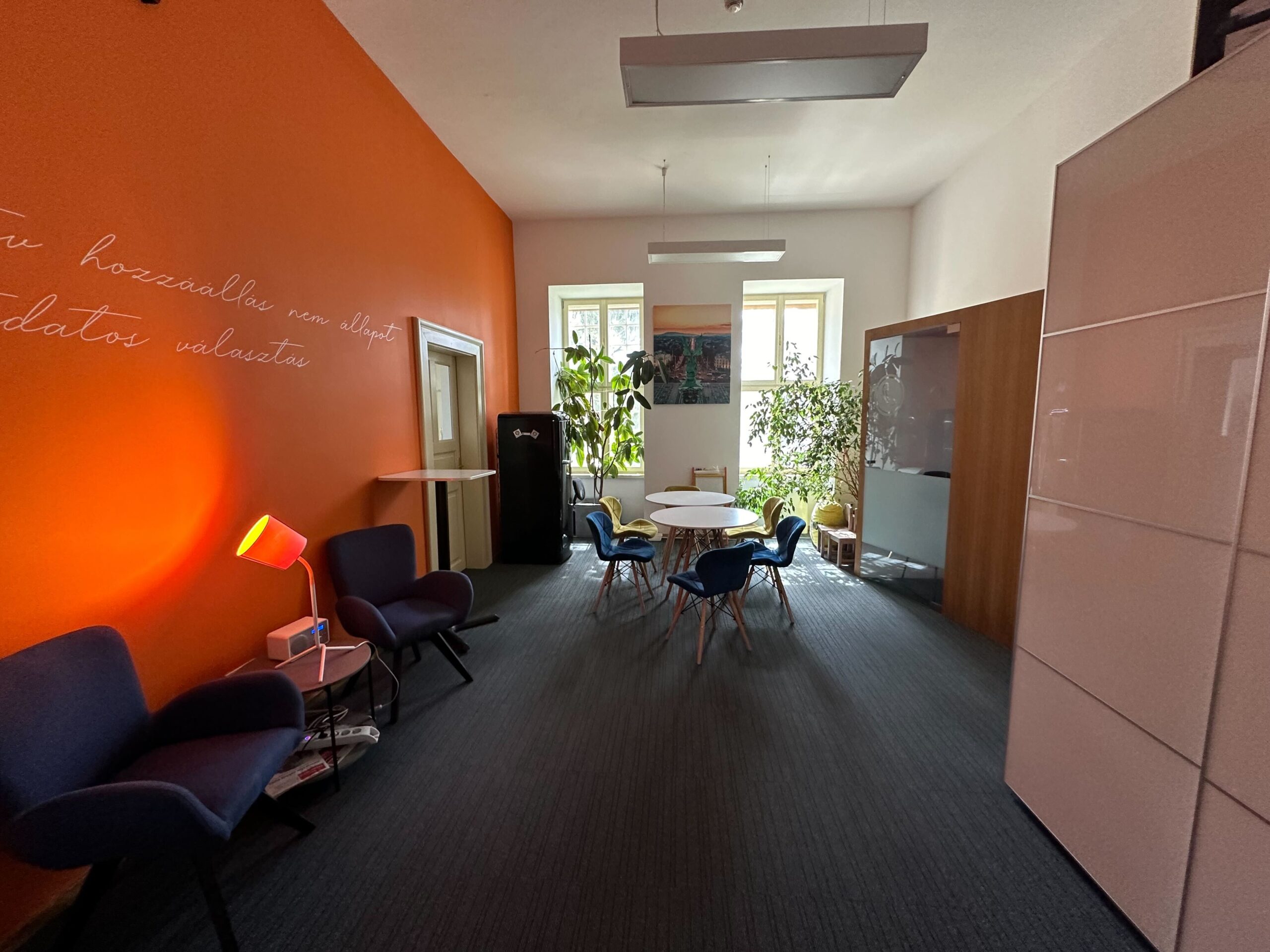 A middle-sized social room with orange wall. chairs and tables.