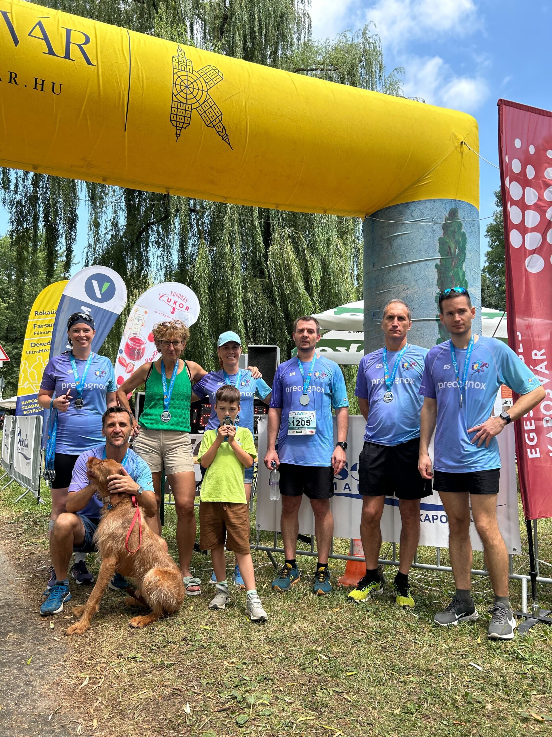 9 people standing in blue t-shirt with a medal on their neck at the end of a running competition.